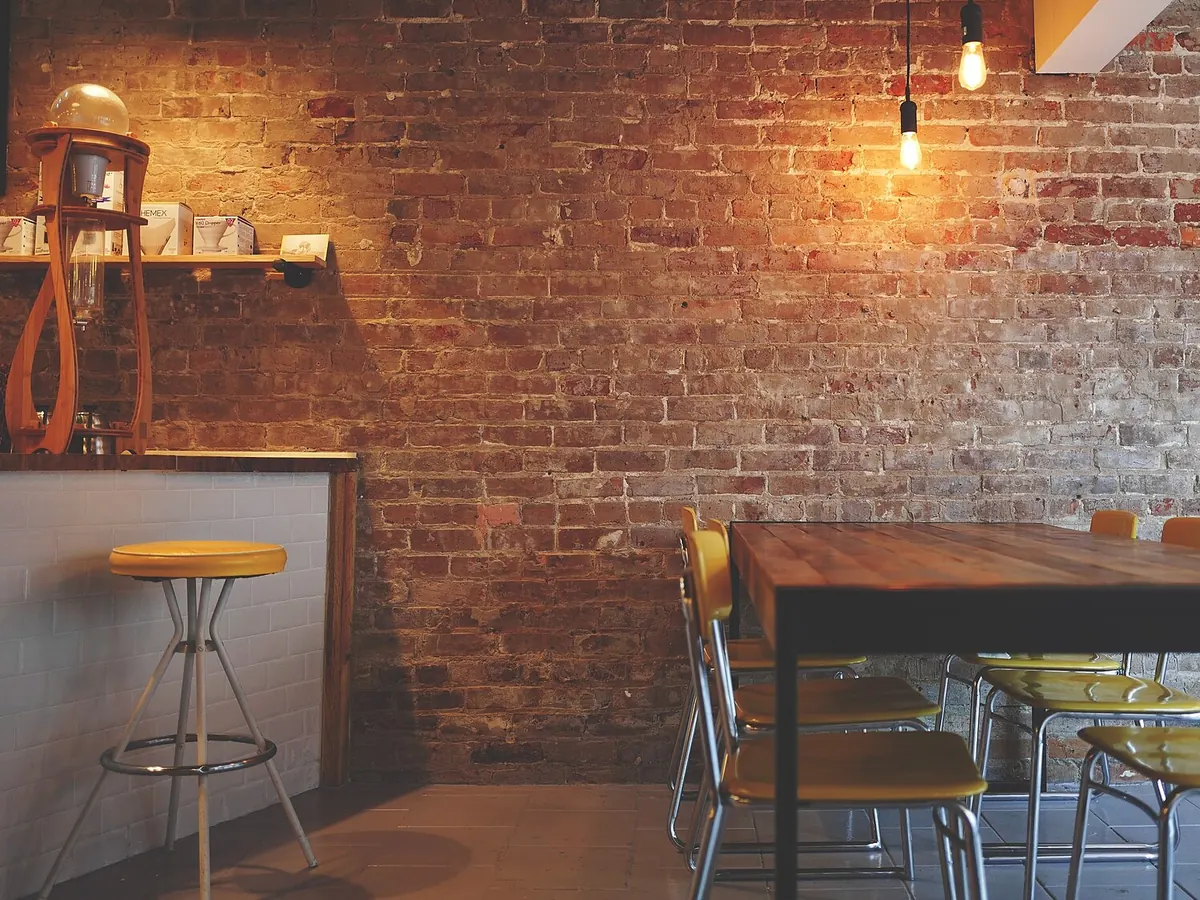 Interior de un local comercial vacío, con mesa, taburetes y pared de ladrillo